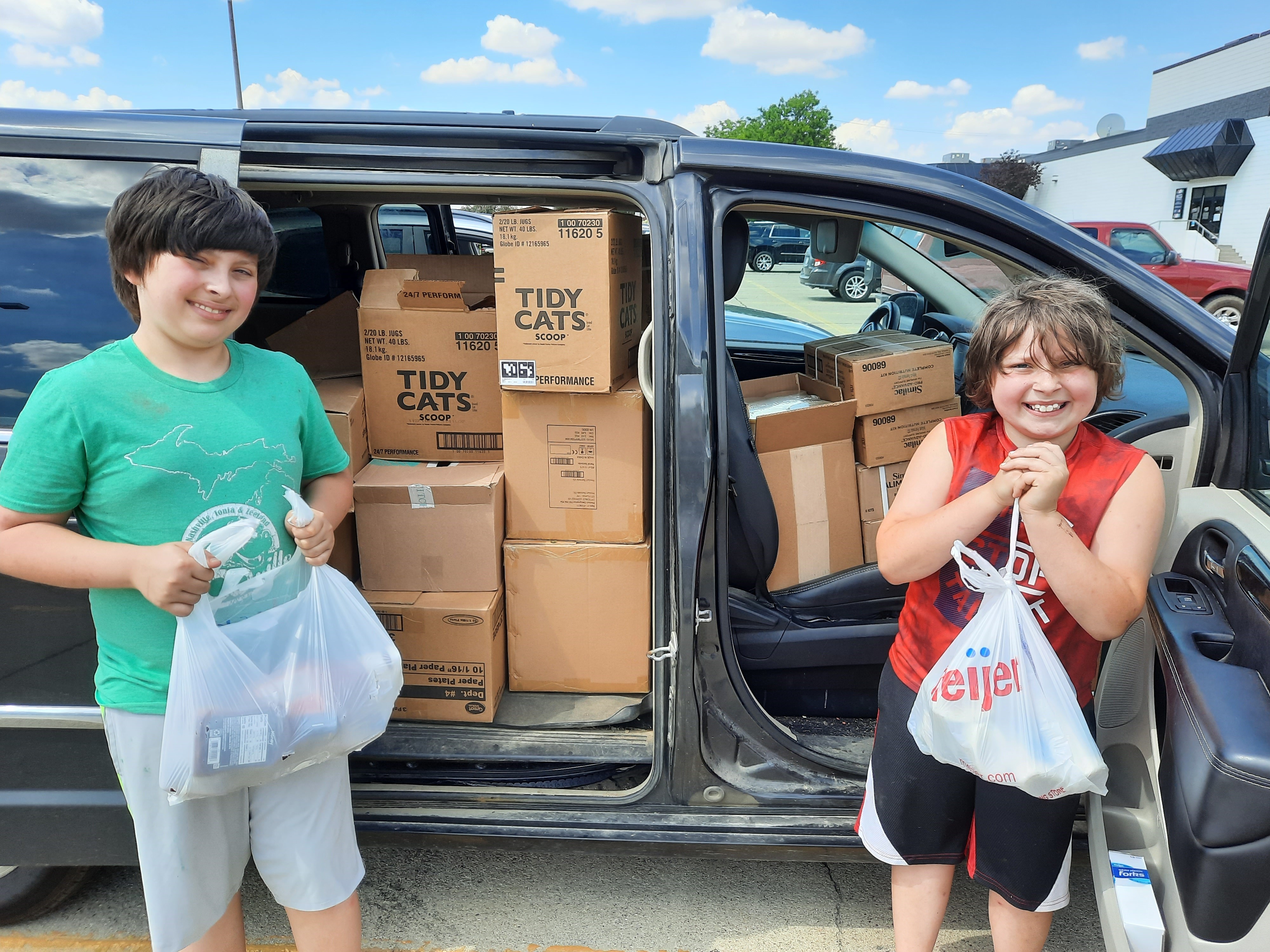 Youth stand next to car full of donated food.